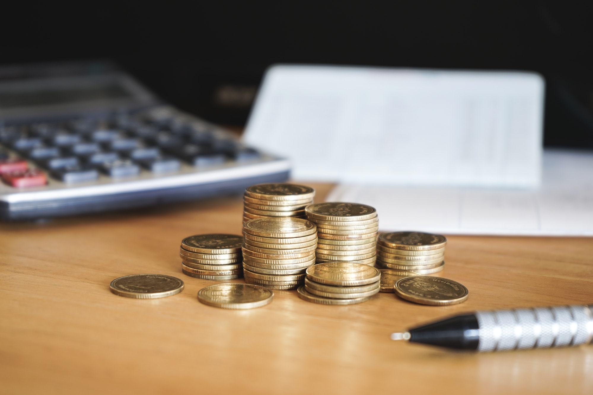 Stack of gold money coin on wood desk with calculator and pen. Business and financial concept